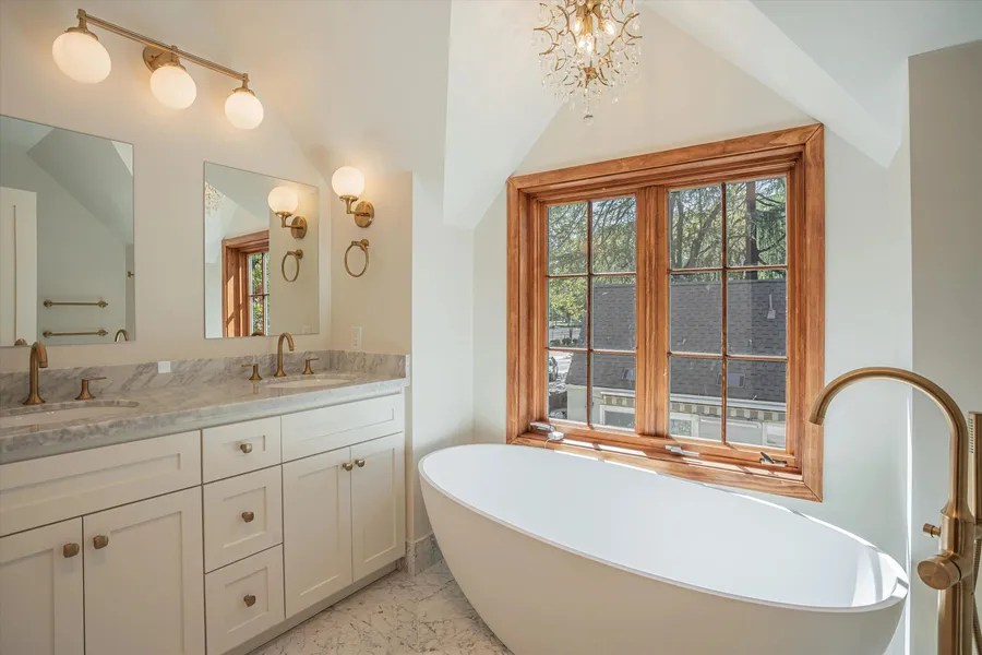 A bathroom with a marble double vanity, brass taps, and a freestanding tub.