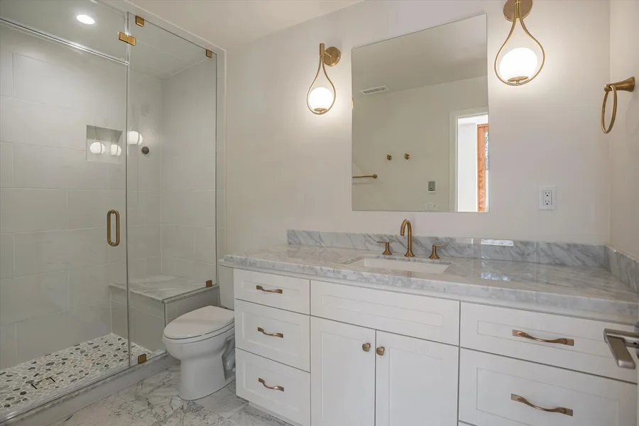 A bathroom vanity with a marble top, brass faucet, and a glass shower.