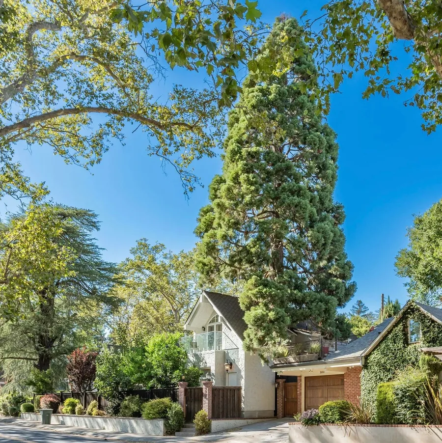A white two-story house beside a tall evergreen, with a brick garage to the right.