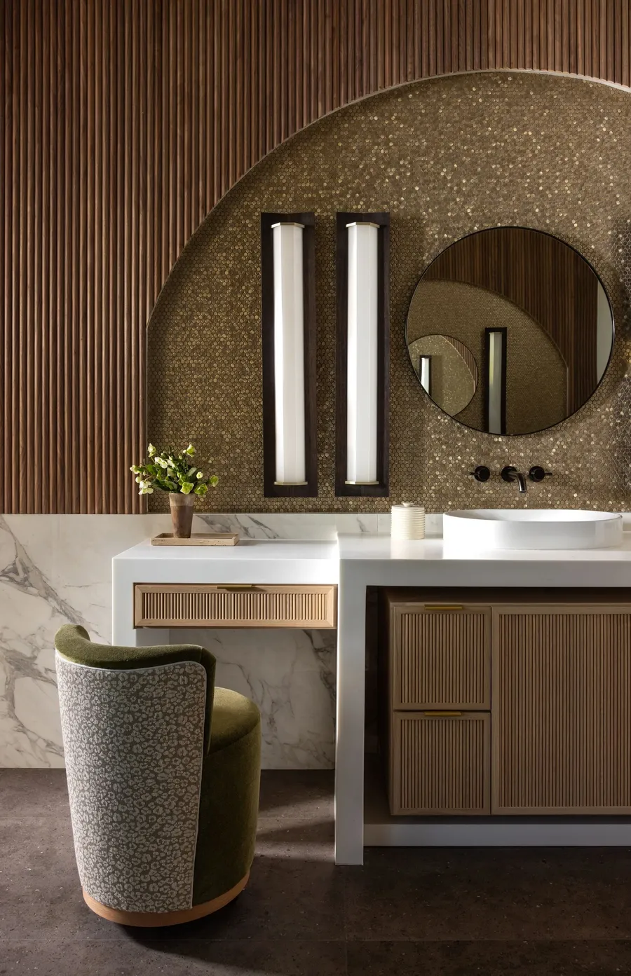 A bathroom vanity set in an arched gold-tile niche with fluted wood drawers.