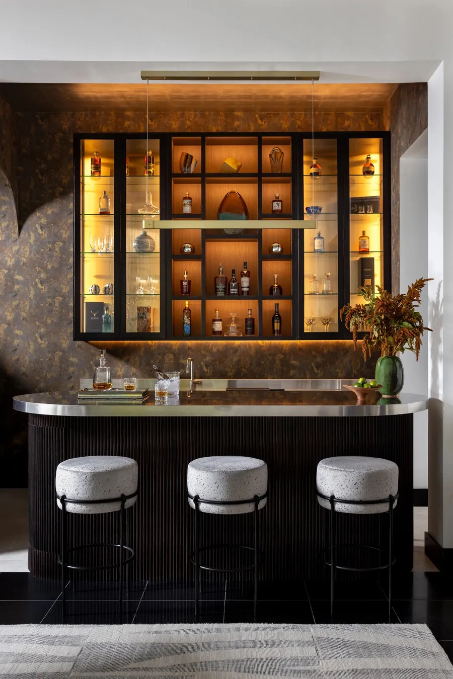 A curved fluted bar with a metal counter and a backlit bottle cabinet.