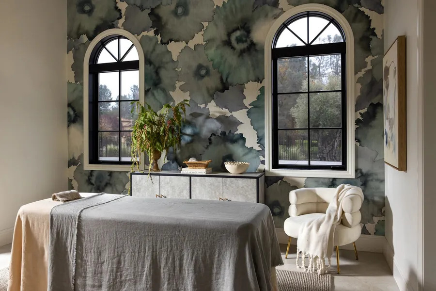 A treatment room with floral wallpaper and two arched windows.