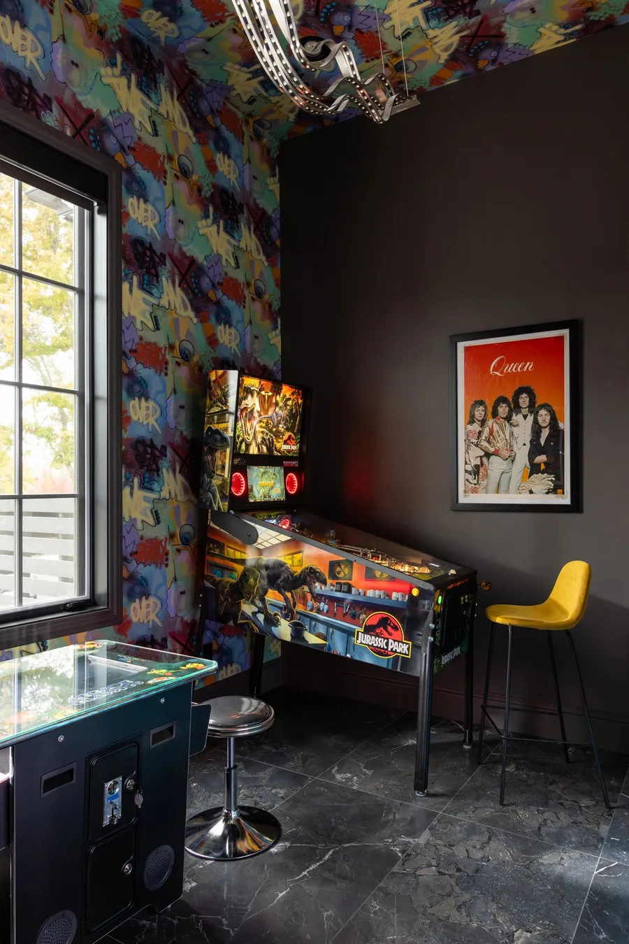 A game room with graffiti wallpaper, marble floors, and a pinball machine.