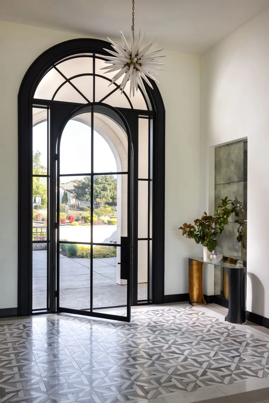 An arched steel-and-glass front door on a geometric tile floor.