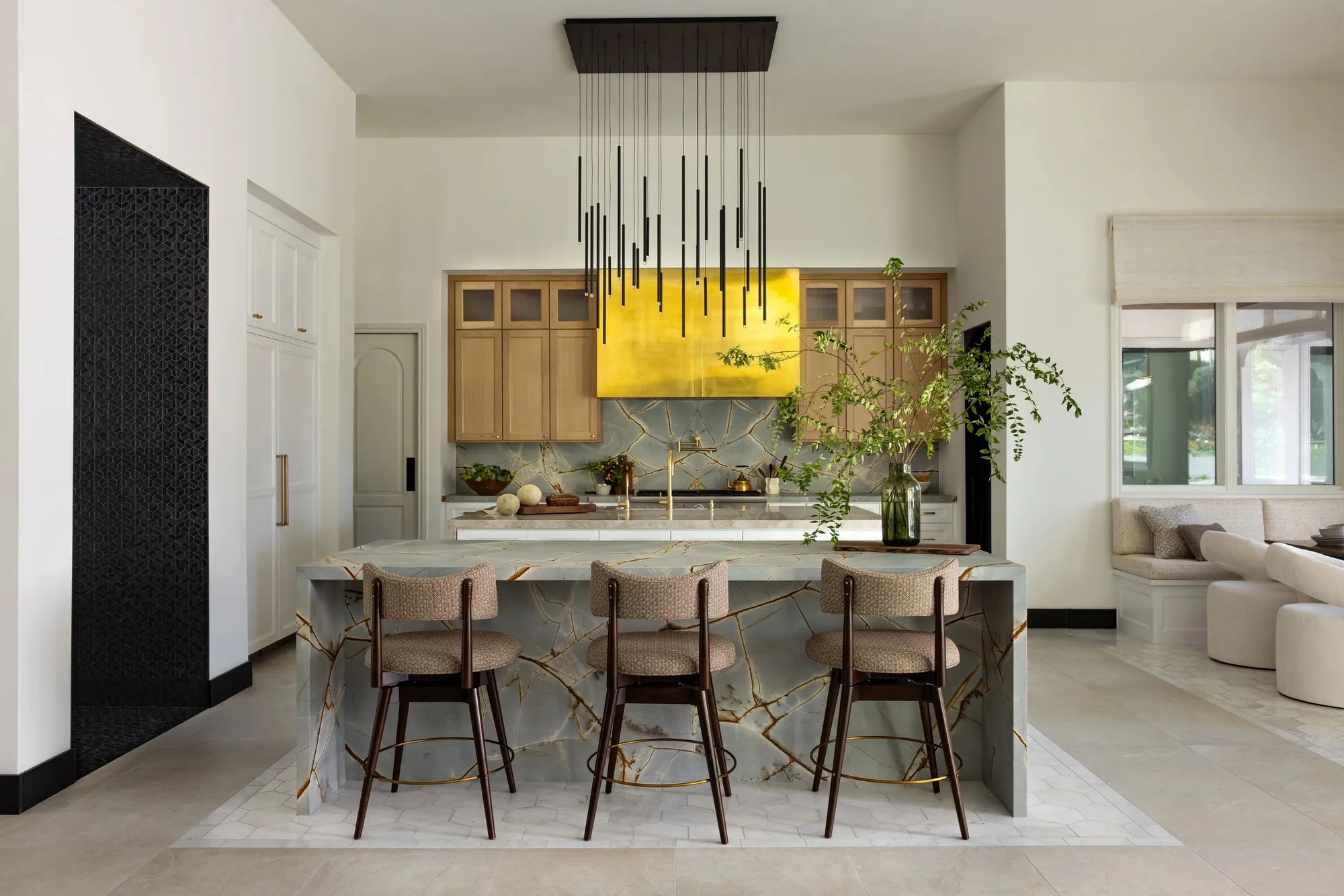 A kitchen with a stone waterfall island, oak cabinets, and a brass range hood.