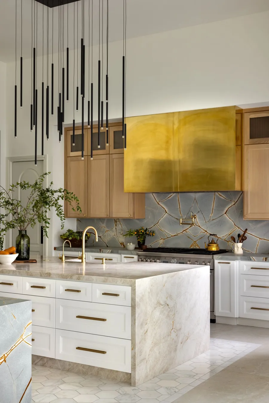 A kitchen island with brass taps and a stone slab backsplash behind the range.